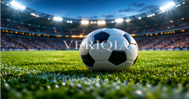 Football resting on stadium grass beneath bright floodlights, colourful landscape editorial photograph with subtle centered VERIQIA watermark